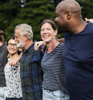 A diverse group of people stand with their arms around eachother.