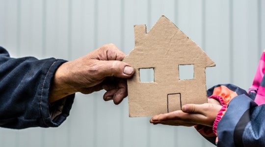 Person handing another person a cardboard cutout of a house. 